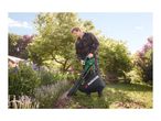 Man using a leaf blower/vacuum in a garden, clearing leaves from a flower bed.