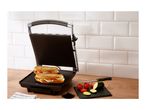 Panini press with two sandwiches, tomatoes, and zucchini on a wooden counter.