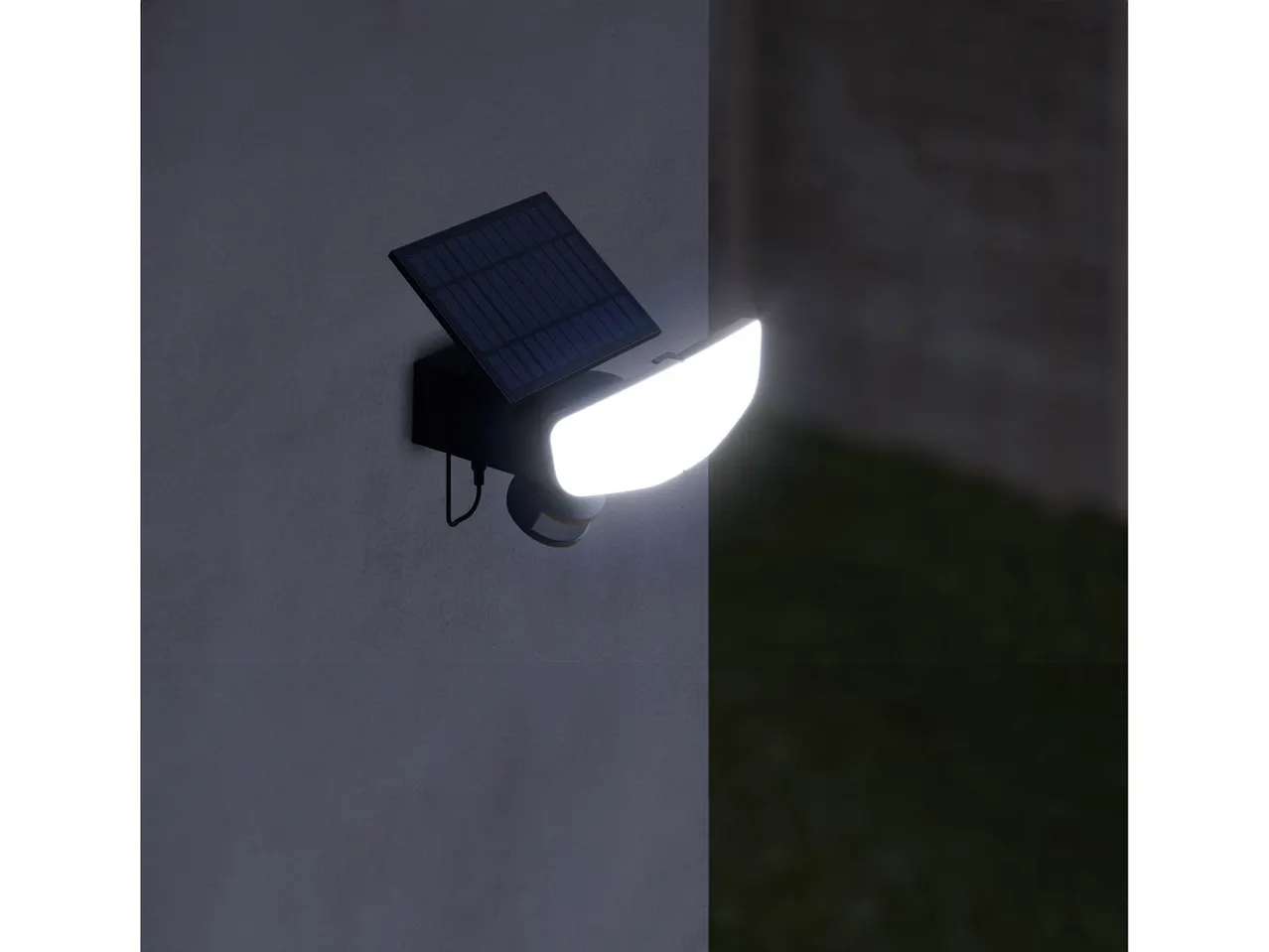 Faretto solare a LED montato su una parete esterna, che illumina un'area scura.