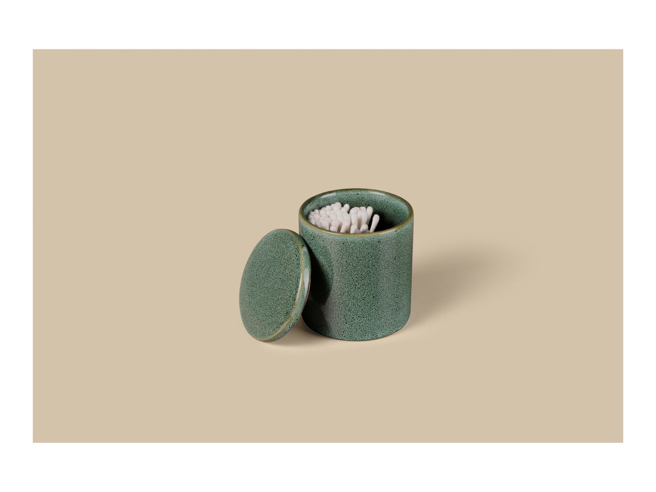 Green ceramic container with lid and cotton swabs on a beige background.