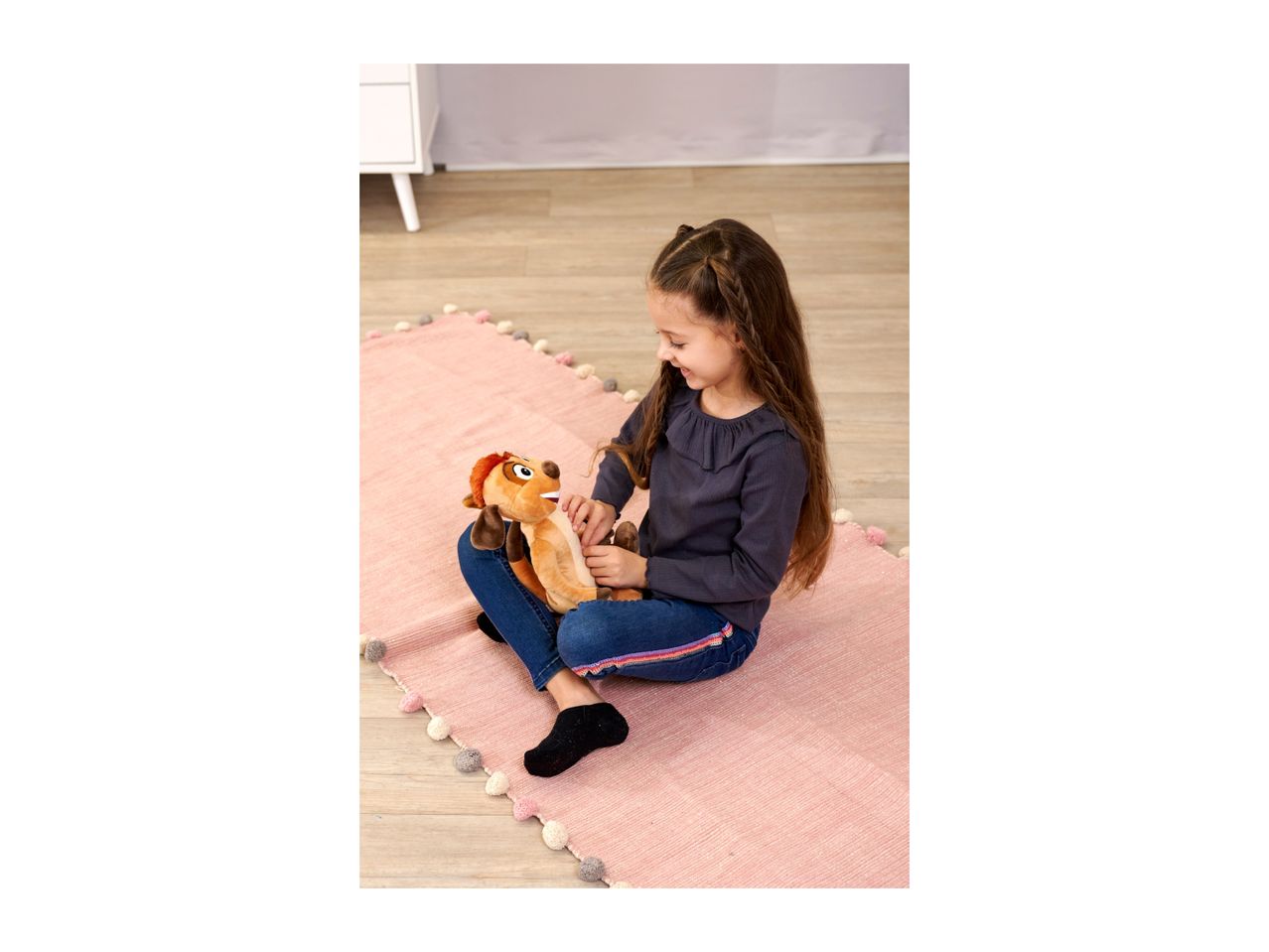 Girl playing with a plush toy on a pink rug.