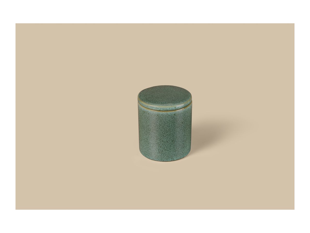 A cylindrical green ceramic jar with a lid, featuring a speckled texture, on a beige background.