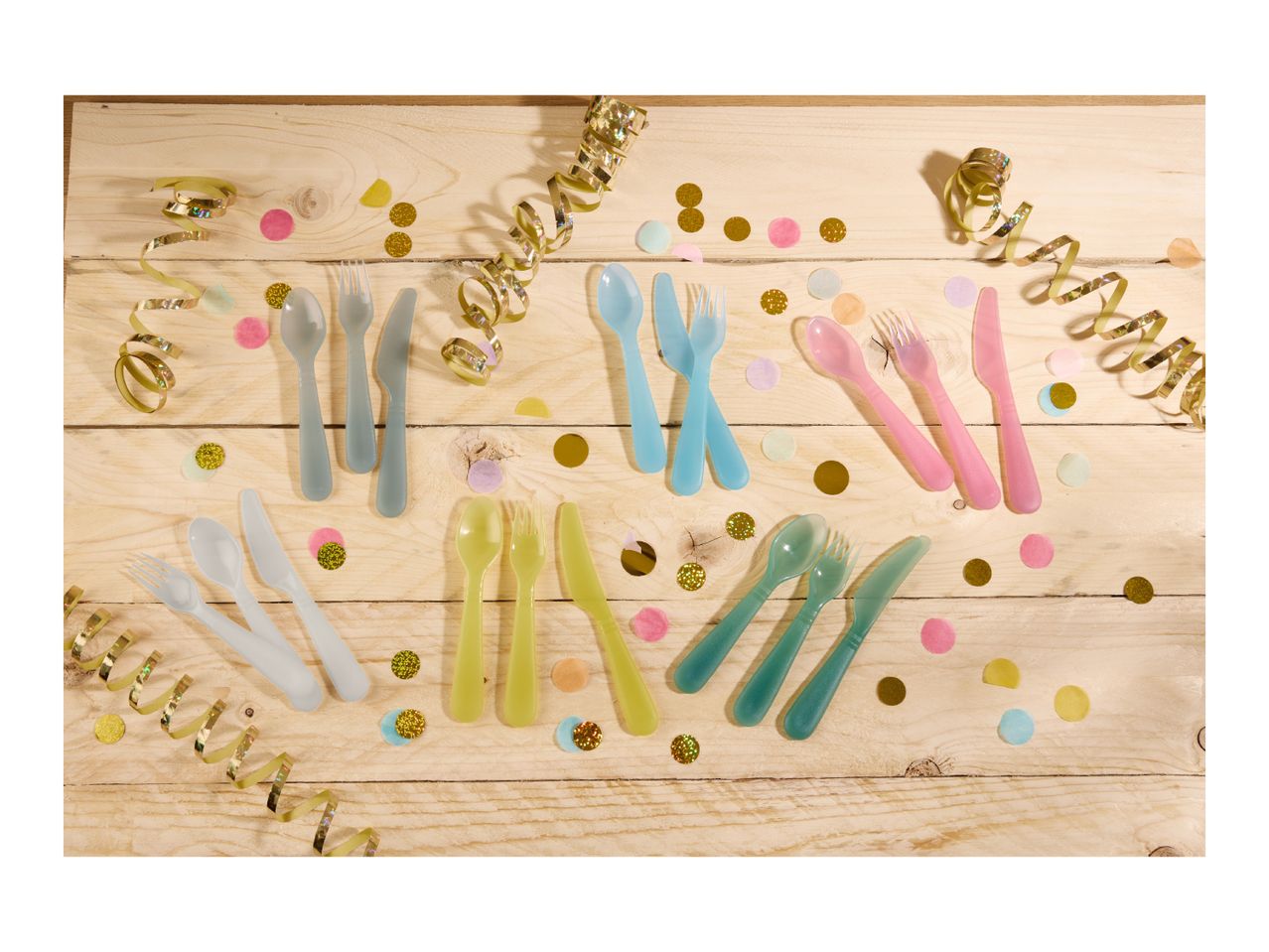 Colorful plastic cutlery sets with confetti and streamers on a wooden table.
