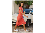 Femme souriante en robe corail et baskets blanches, marchant avec une tasse réutilisable.