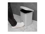 Foot opening a white pedal bin with a black inner bucket, against a grey tiled wall.