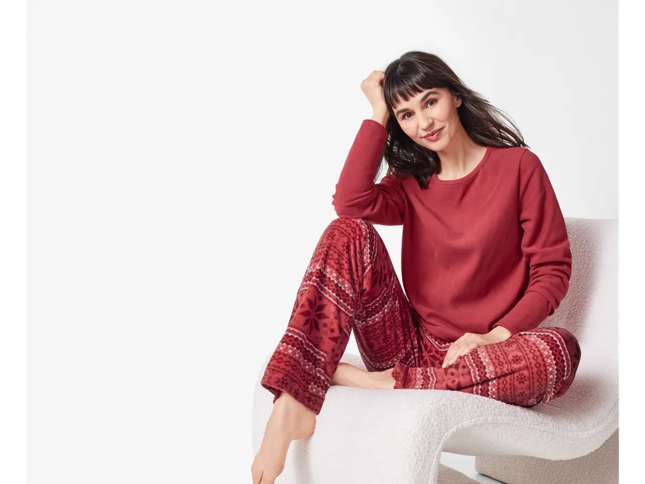 Woman in red fleece pyjamas with a snowflake pattern, sitting on a white chair.