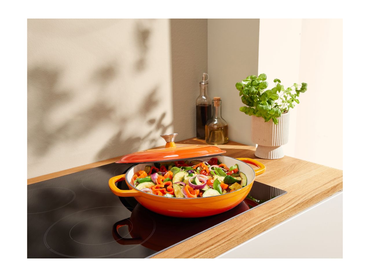Orange Le Creuset Dutch oven with vegetables on an induction cooktop.