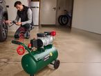 Un uomo gonfia il pneumatico di un'auto con un compressore d'aria Parkside verde in un garage.