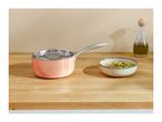 Pink saucepan with lid, bowl of soup, and olive oil bottle on a wooden counter.