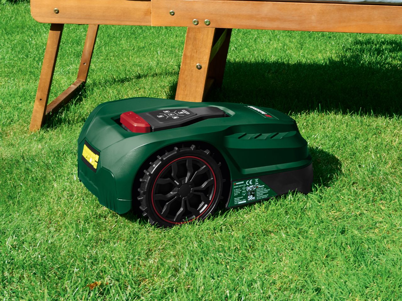 Robotic lawnmower on green grass under a wooden bench.