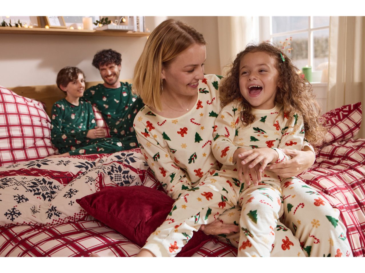 Family in matching Esmara Christmas pyjamas, laughing on a festive bed.