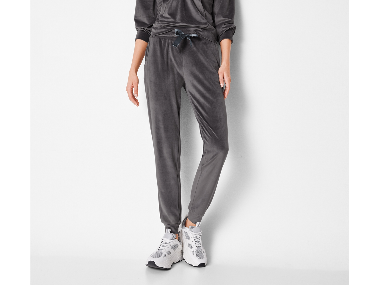 Žena nosi sivi Nicki-Hoodie i odgovarajuće donje delove trenerke sa belim patikama.