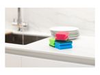 Colorful kitchen sponges on a white countertop next to a sink and stacked plates.
