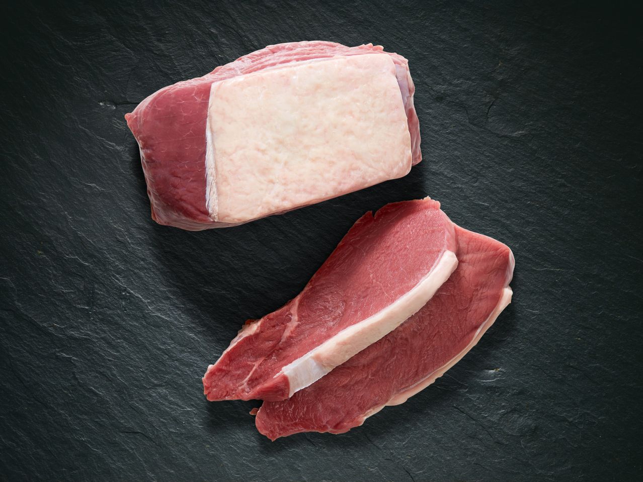 Zwei Stücke rohes Fleisch auf einer schwarzen Oberfläche.