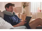 Um homem relaxa na cama com um travesseiro de pescoço, lendo um livro.
