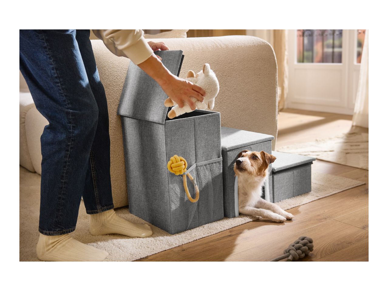 Grey fabric pet stairs with built-in storage compartments and a small dog looking out.