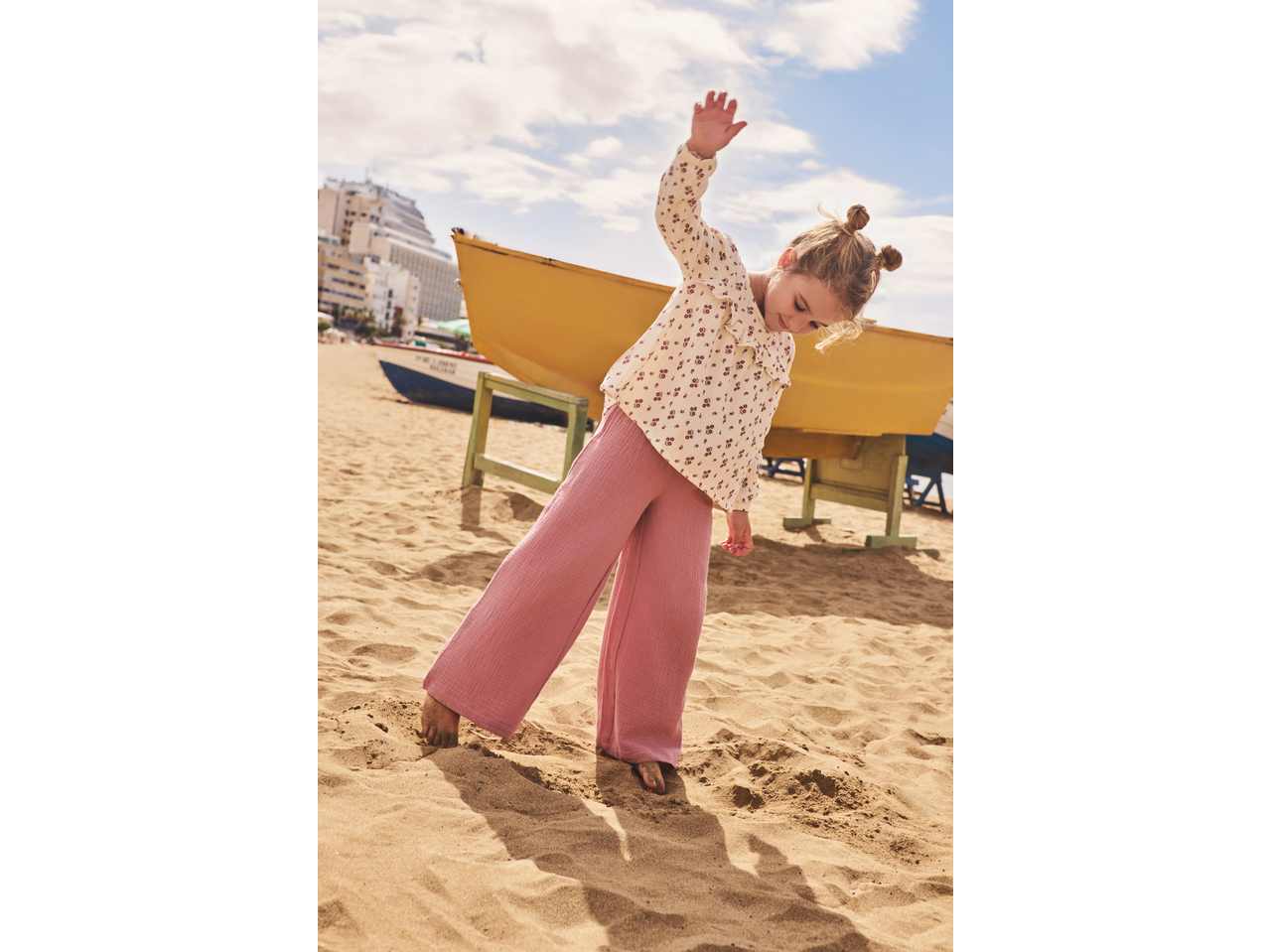 Fetiță în pantaloni de muselină roz LUPILU jucându-se pe plajă.