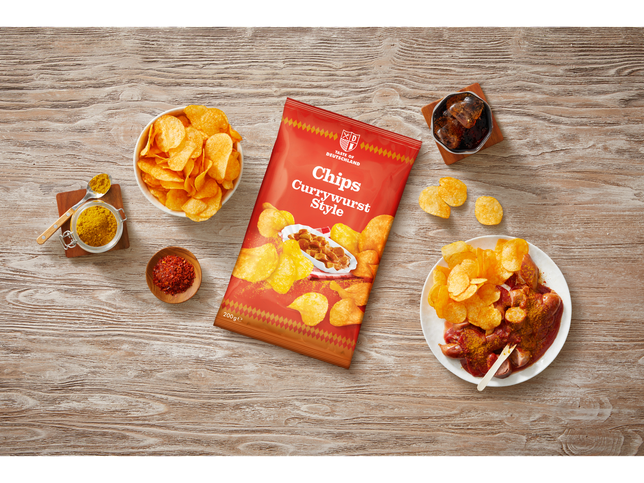 Currywurst-stijl chips in een zak en kom, met currywurst en kruiden op een houten tafel.