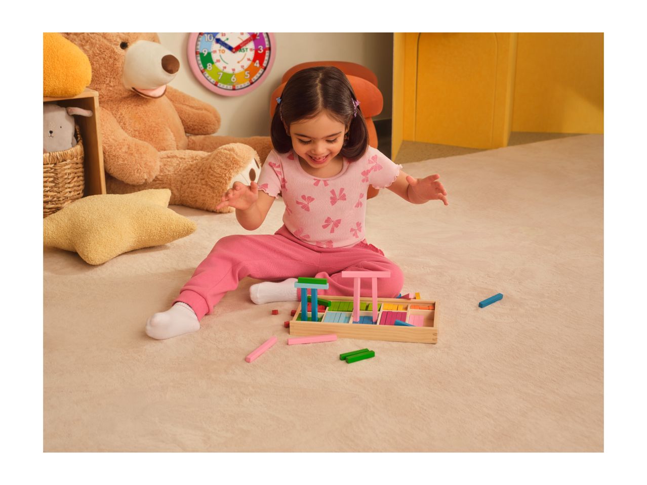 A young girl playing with colorful wooden blocks on a rug, surrounded by toys.