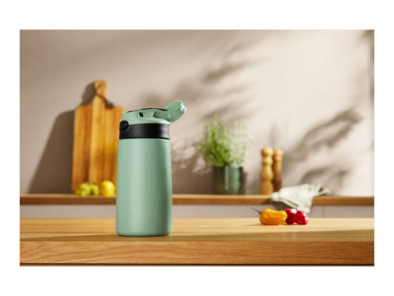 Mint green water bottle on a wooden kitchen counter with fruit and peppers.