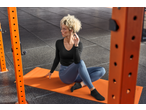 Woman in black long-sleeve top and blue leggings sitting on an orange yoga mat.