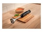 Black hand blender on a wooden cutting board next to a bowl of tomato soup