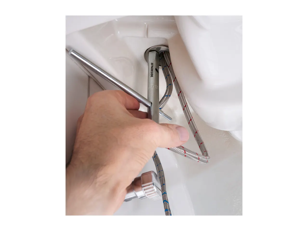 A person's hand using a basin wrench to tighten a faucet connection with braided hoses.
