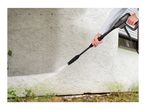 Person cleaning a textured wall with a pressure washer, removing green algae.