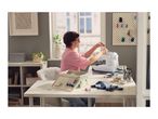 A woman using a white sewing machine at a desk with sewing accessories.