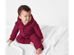 Baby in lupilu® merinowollen jumpsuit op een witte deken.