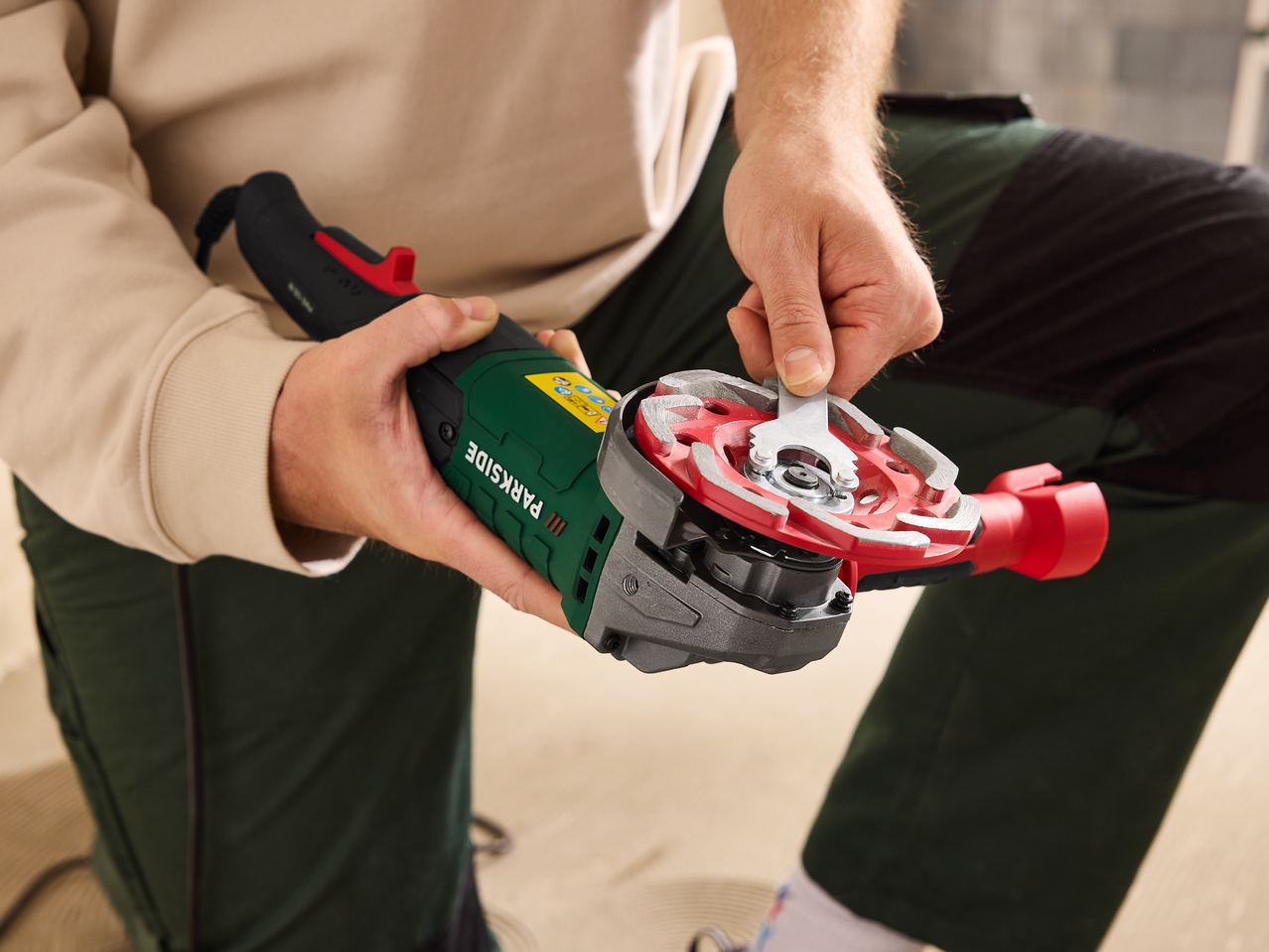 Κοντινό πλάνο χεριών που ρυθμίζουν έναν δίσκο λείανσης σε γωνιακό τροχό με κλειδί.