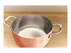 Copper-colored cooking pot with stainless steel interior and measurement markings on a wooden surface.