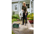 Woman pressure washing a garden path with a green pressure washer and foam sprayer.