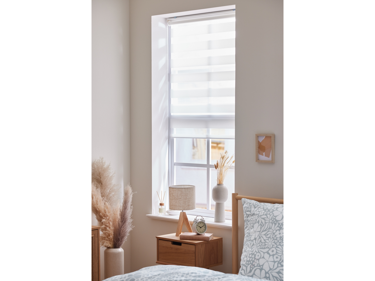 Spavaća soba sa drvenim noćnim ormarićem, lampom, budilnikom i krevetom sa cvetnom posteljinom.