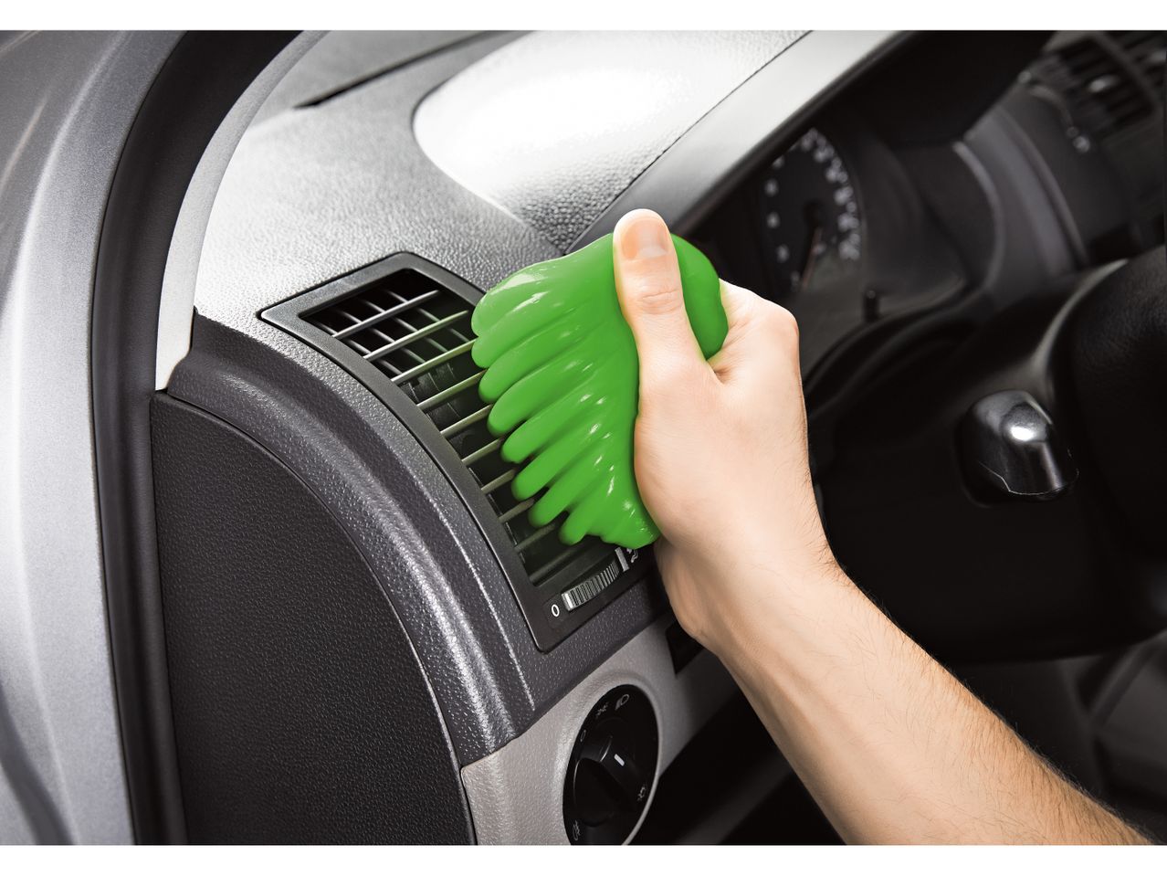 A hand uses a green cleaning gel to clean a car's air vents.