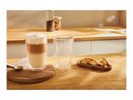 Latte macchiato in a double-walled glass, an empty glass, and biscotti on a wooden counter.
