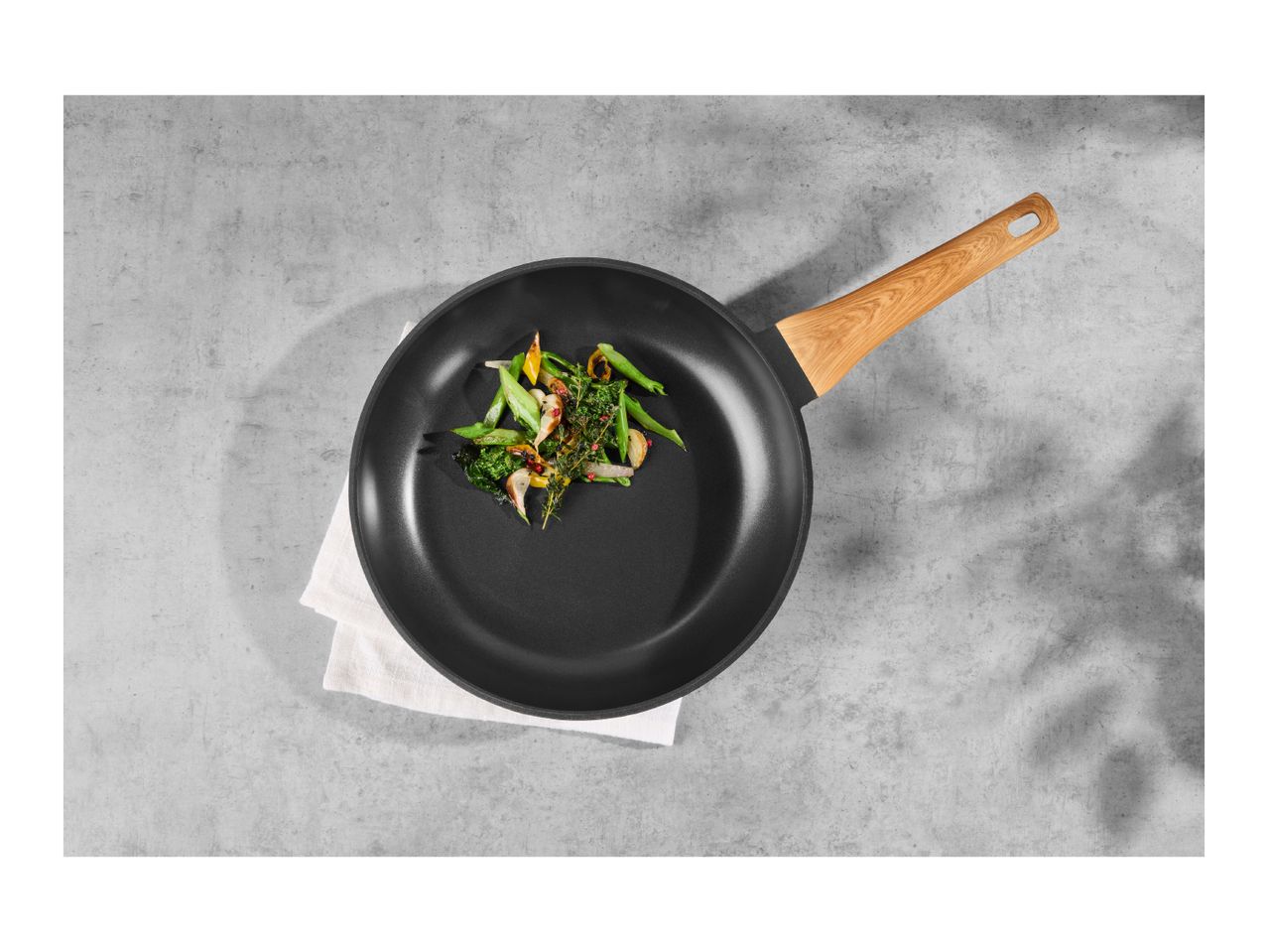 Overhead shot of a black frying pan with a wooden handle, containing sautéed vegetables.