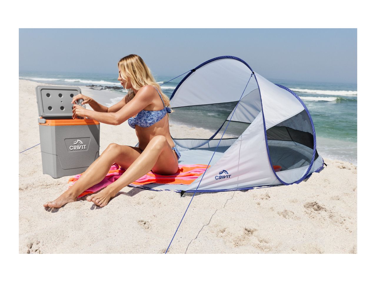 Woman on a beach opening a cooler next to a beach tent.