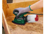 Mão enluvada a usar uma lixadeira Parkside com caixa de pó numa superfície de madeira.