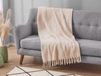 A gray sofa with a light beige throw blanket draped over it, next to a vase with pampas grass.