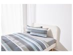 A bed with a striped duvet cover and pillows in a bright room with white curtains.