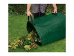 Person emptying a green garden waste bag filled with leaves onto a lawn.