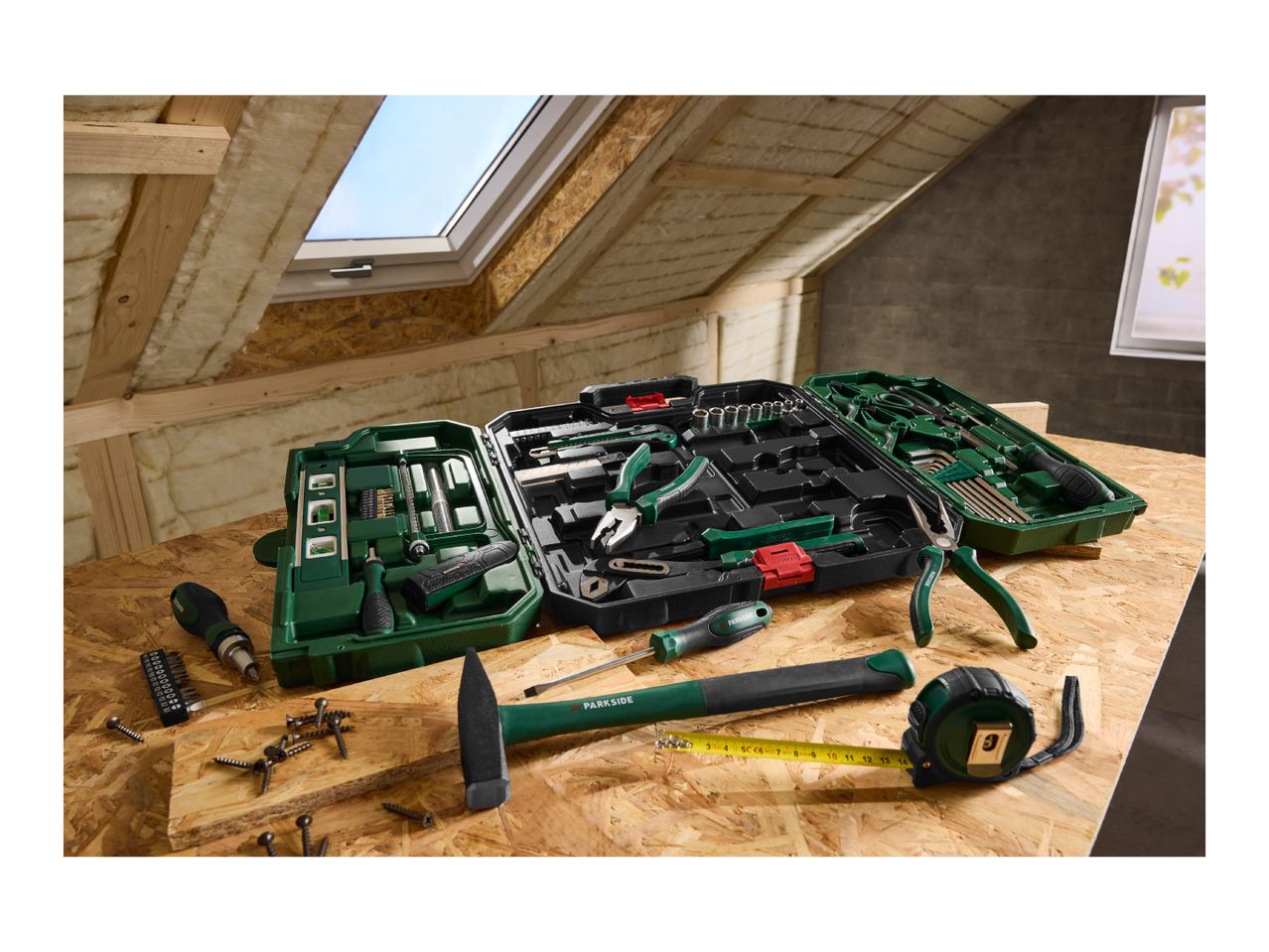 A comprehensive toolkit with various hand tools, including screwdrivers, pliers, a hammer, and a tape measure, on a wooden surface in an attic.