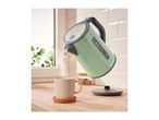 A green Silvercrest kettle pouring water into a beige mug on a wooden counter.