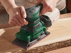 A person uses a Parkside brand electric sander on a piece of wood.