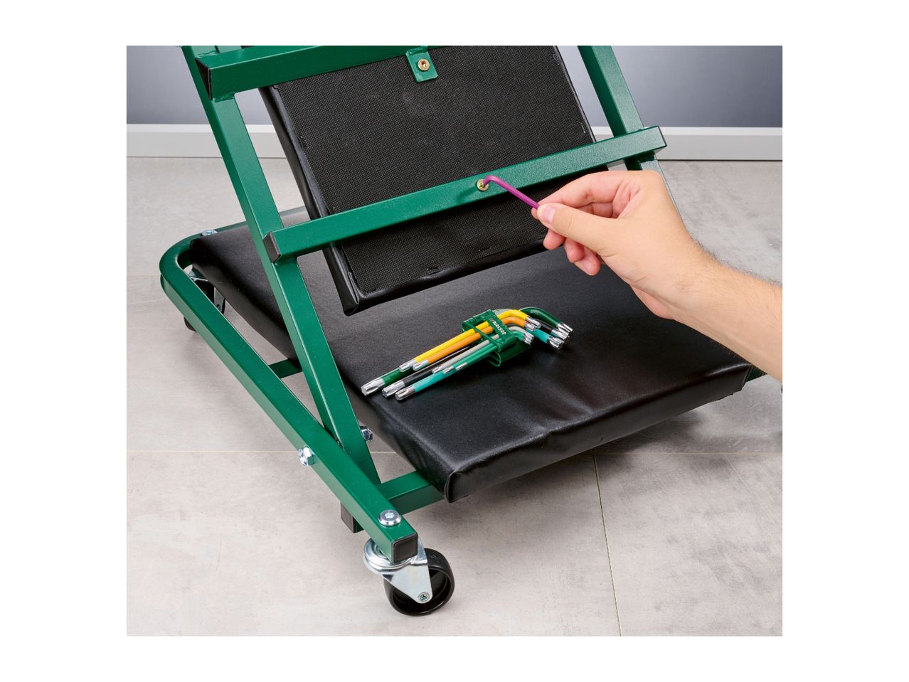 A person assembling a green workshop creeper with an Allen key, with a set of hex keys on the seat.