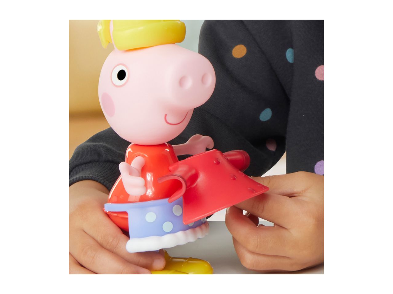 Child playing with a pig character toy, dressed in a red outfit with a blue and white skirt.