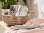 A woven basket holds razors and other bath items on a soft pink blanket.