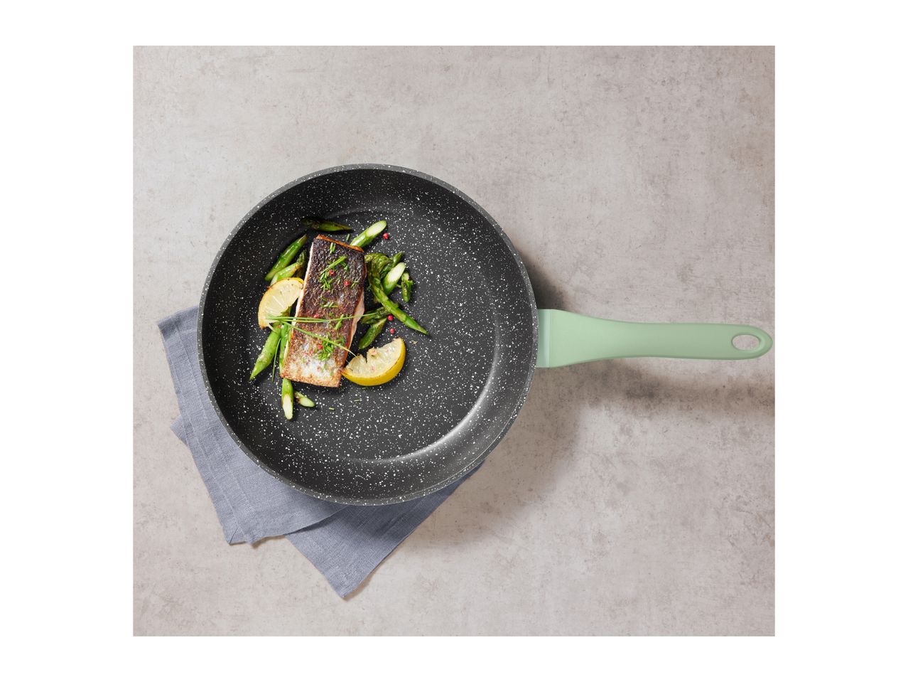 Frying pan with salmon, asparagus, and lemon on a grey background