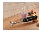 Black hand blender on a wooden countertop next to a beaker with a purple smoothie